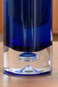 Two blue cylindrical glass vases on a wooden surface with a dark background